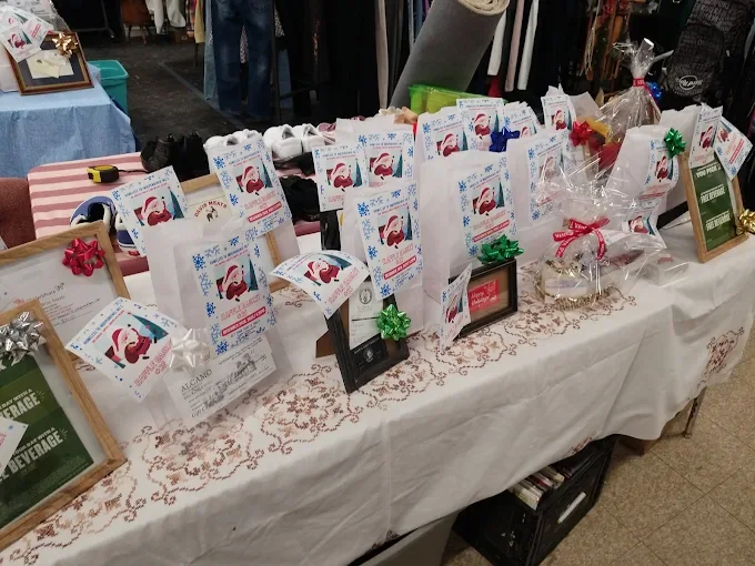 a table set up inside quakertown farmers market with several small white bags featuring a santa claus design, likely for a holiday raffle or giveaway.