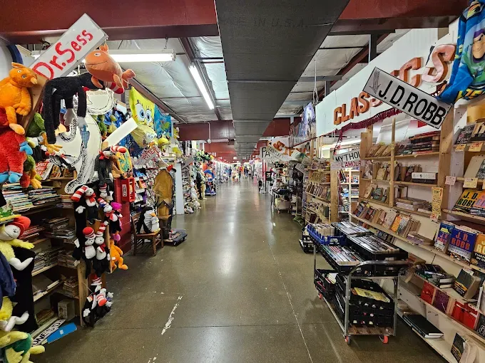 a wide aisle in a bookstore, shelves filled with colorful books and plush toys, including dr. seuss characters and more at caesar creek flea market