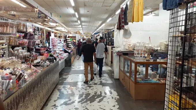 old paris flea market at a t aisle features stalls with hanging clothes, accessories, and decor items. shoppers casually walk through the lively, cluttered space.