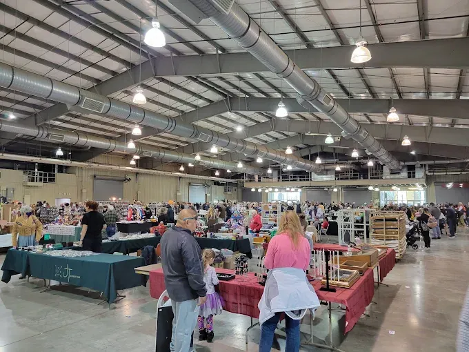 tulsa flea market with high ceilings and exposed ductwork. crowds browse various booths with items on red and green tablecloths. busy