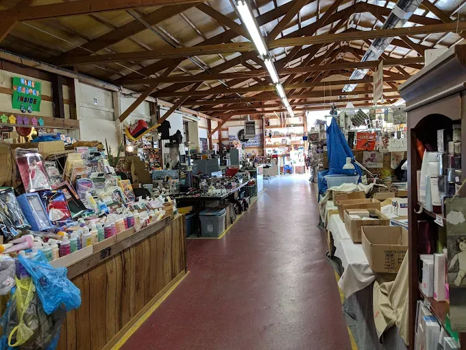 a jamie's flea market aisle with wooden beams and red flooring, lined with diverse goods and crafts,
