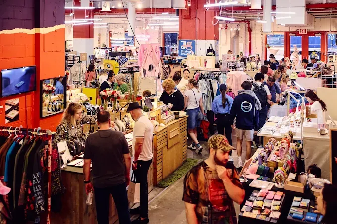 a bustling, colorful pop-up market with shoppers exploring clothing and accessories. warm lighting and vibrant decor create a lively and energetic atmosphere.
