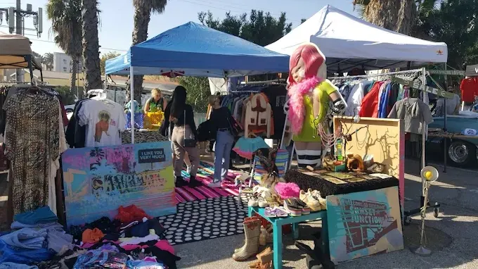 a vibrant outdoor scene at the silverlake flea market in pennsylvania, showing vintage clothing racks, local art, and shoppers under blue tents on a clear, sunny day.