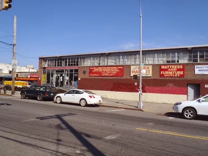 street view of a brick building housing a flea market and mattress outlet, with cars parked along the road. bright signage adds a vibrant feel.