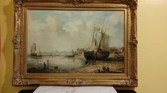 a classical oil painting in an ornate gold frame depicting sailing ships in a harbor.