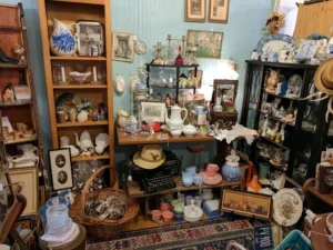 a cluttered antique shop corner filled with vintage items like a typewriter, ceramic dishes, framed photos, glassware, and decorative plates. warm, nostalgic ambiance.