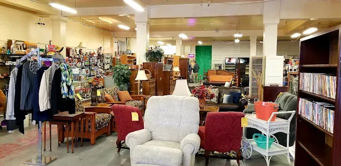 a spacious thrift store interior filled with assorted furniture and decor items; shelves display books and clothes, creating a cozy, eclectic vibe.
