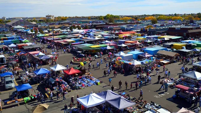 aerial view of a bustling outdoor market with rows of vibrant canopies. crowds of people browse diverse stalls under a clear blue sky, creating a lively atmosphere.