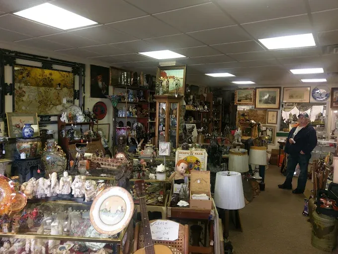 an antique shop interior filled with decorative figurines, lamps, framed art, and various vintage collectibles.