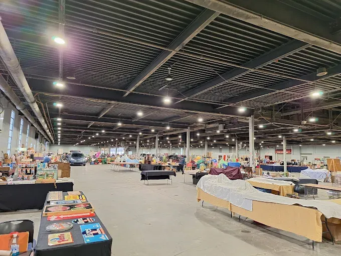 an expansive indoor event space with long tables arranged for a market or fair under a dark ribbed ceiling.
