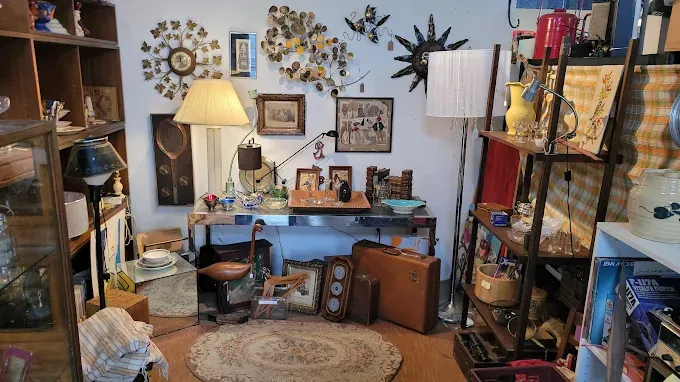 at benningtons antique center a cluttered thrift store aisle featuring shelving units with kitchenware, a large yellow lego head, and a pair of white sneakers on a chair