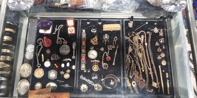 at kentucky flea market a glass display case filled with vintage jewelry, pocket watches, medals, and small trinkets.