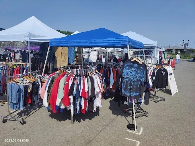Circular racks of t-shirts and jackets under a blue canopy at the lucky flea market.