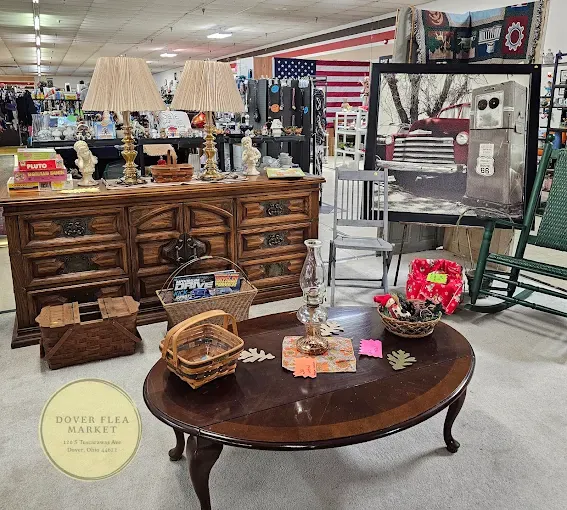 dover flea market booth with wooden furniture, including a dresser with two lamps and figurines, and a coffee table with decor. a rustic photo and various items create a nostalgic atmosphere.