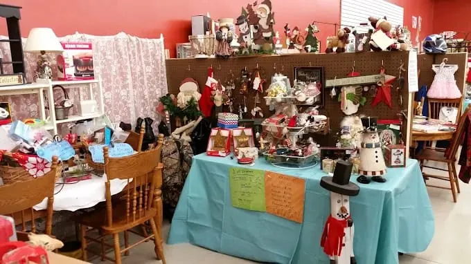 festive craft store display with holiday decorations on tables and shelves. includes snowman figures, ornaments, and vibrant signs on a turquoise tablecloth at funky munky flea market.