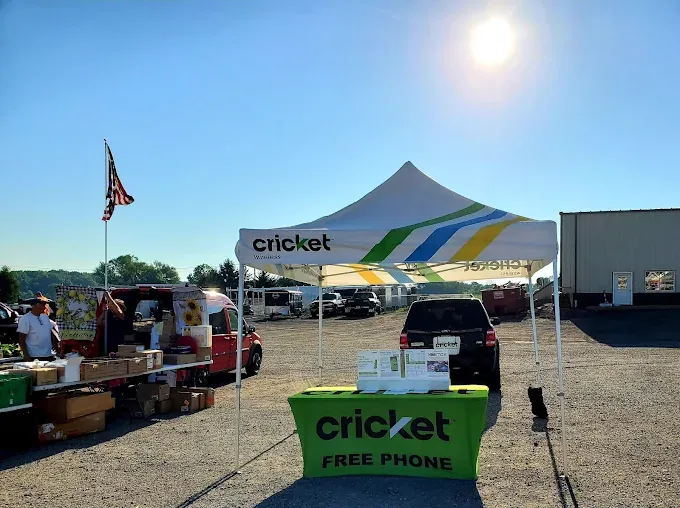 outdoor market scene under a clear blue sky with a bright sun. a cricket wireless booth, offering free phones, features a colorful canopy and display at the the heritage market place
