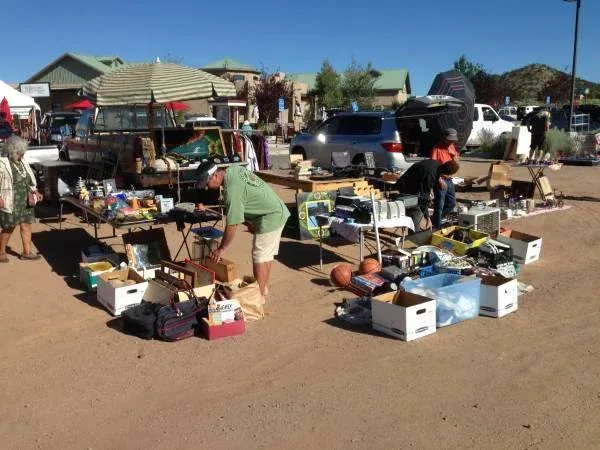 the flea at la tienda with sunny skies, tables filled with assorted items like books, dishes, and toys. shoppers browse, creating a lively, bustling scene.